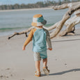 Child walking on a beach with driftwood in the background
