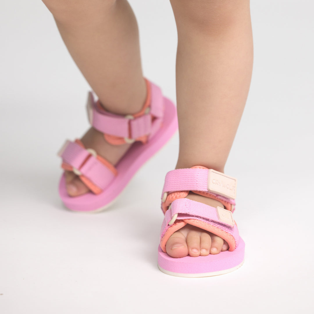 Pink and orange crywolf beach sandals worn by a child on a light gray background
