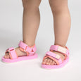 Pink and peach beach sandals worn by a child on a light gray background