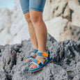 Child wearing crywolf blue sandals with orange accents on a rocky surface