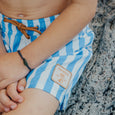 Close-up of a child wearing crywolf blue and white striped  board shorts with a brand logo on a textured surface.