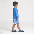 Child wearing a crywolf blue long-sleeve rash vestand striped board shorts on a white background