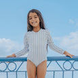 Young girl in a striped crywolf swimsuit standing on a balcony with a blue sky background
