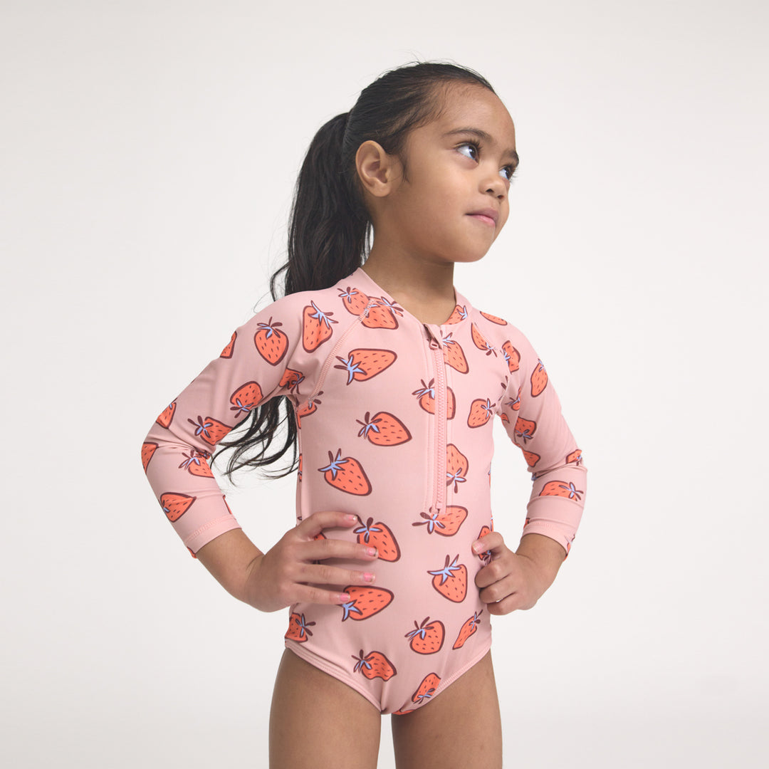 Young girl wearing a Crywolf pink swimsuit with strawberry pattern on a white background