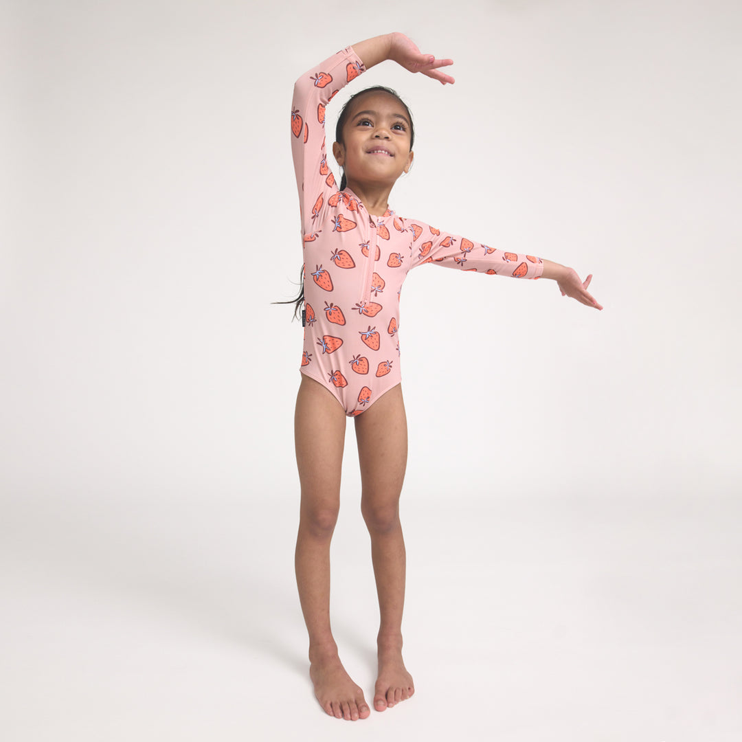Young girl in a pink crywolf swimsuit with strawberry pattern on a white background