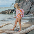 Person wearing a pink crywolf swimsuit with orange patterns and a matching cover-up on a beach.