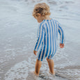 Child wearing a crywolf blue and white striped swimsuit standing in shallow water at the beach.