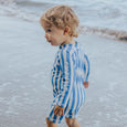 Child wearing crywolf blue and white striped swimsuit standing on a beach.