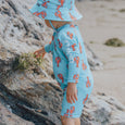 Crywolf child wearing a blue swimsuit with orange patterns and matching hat on a rocky beach.
