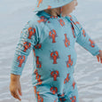 Crywolf Child wearing a blue swimsuit with red lobster pattern by the water