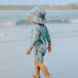 Child wearing a Crywolf blue and orange swimsuit with a matching hat on a beach.