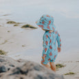 Crywolf Child wearing a blue swimsuit with red patterns and matching hat on a beach.