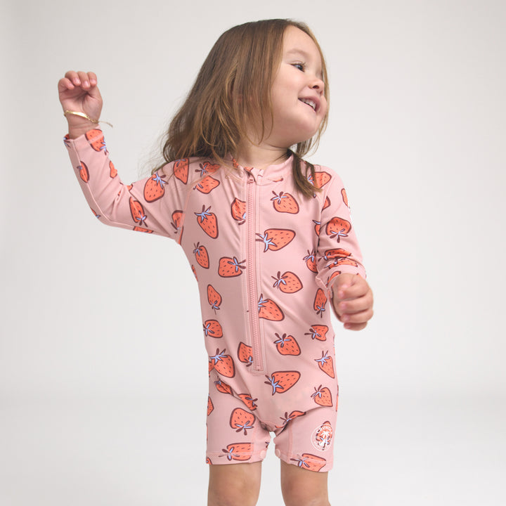 Crywolf Child wearing a pink strawberry-patterned onesie on a white background
