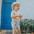 Child in crywolf blue and white striped swim nappy holding an apple outdoors.
