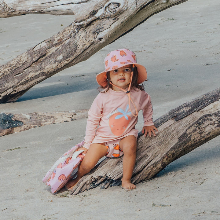 Child in a pink crywolf outfit and hat sitting on a log at the beach