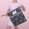 Person holding a dark gray pouch with pink cherry pattern against a pink background