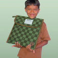 Child holding a green checkered bag with a visible brand label against a light green background