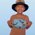 Child wearing a blue hat and brown shirt holding a blue pouch with whale design on a light blue background