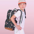 Child wearing a large black backpack with pink details on a pink background