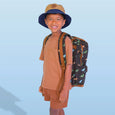 Child wearing a brown shirt, shorts, and a blue hat with a dinosaur-patterned backpack on a light blue background