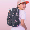Child wearing a gray backpack with pink floral patterns on a pink background