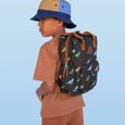 Child wearing a dinosaur-patterned backpack against a light blue background