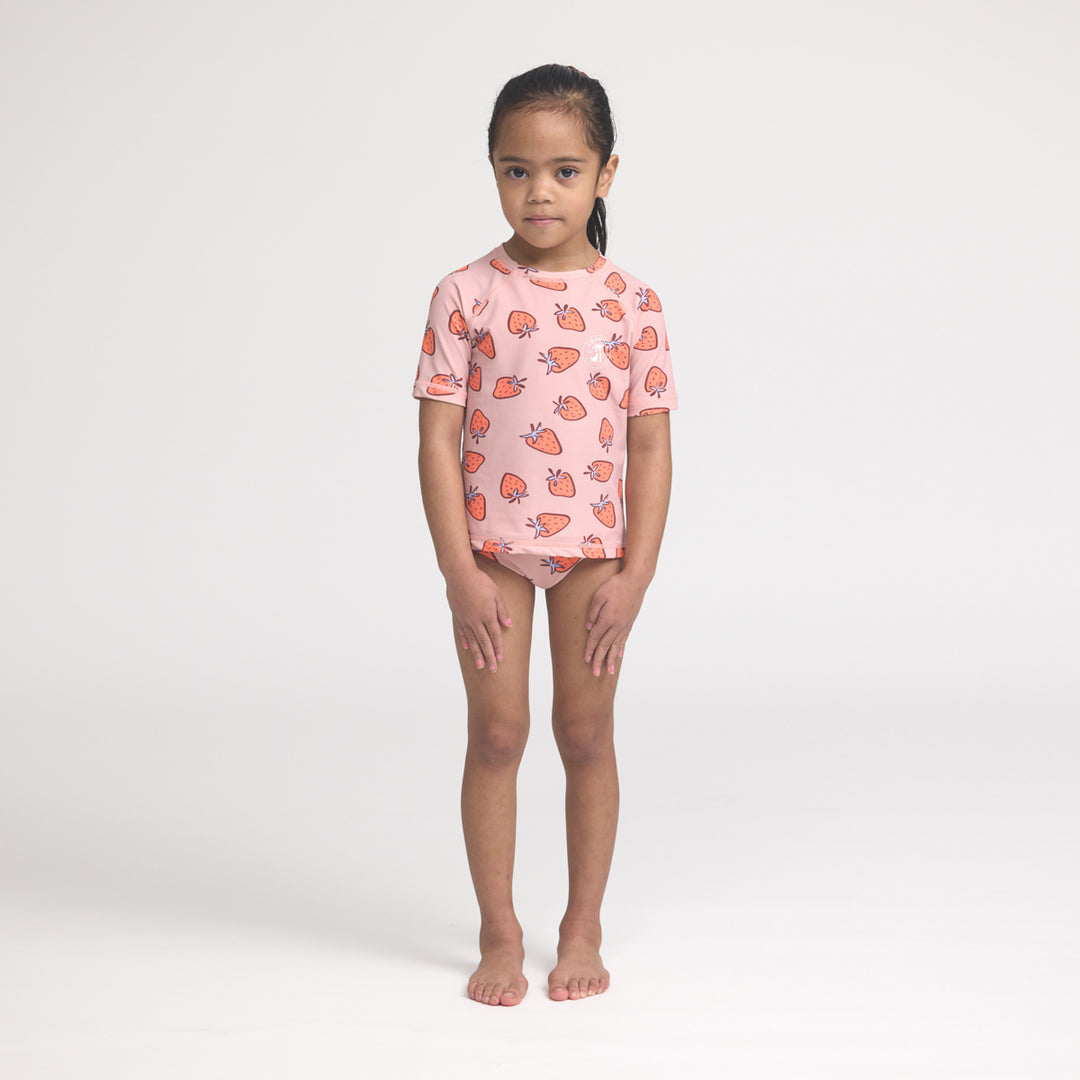 Young girl wearing a crywolf pink rash set with strawberry pattern on a white background