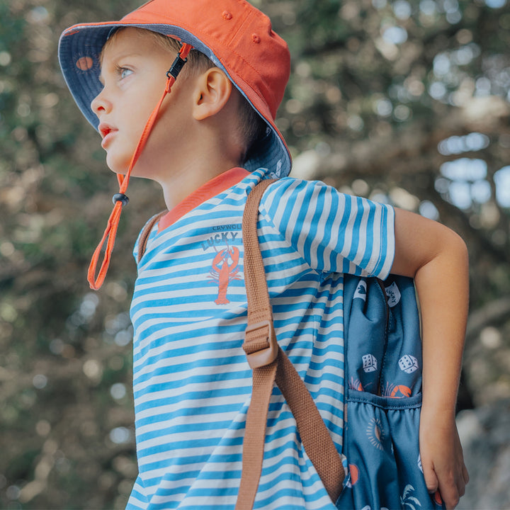 Child wearing a crywolf striped tee and orange bucket hat with a blurred natural background