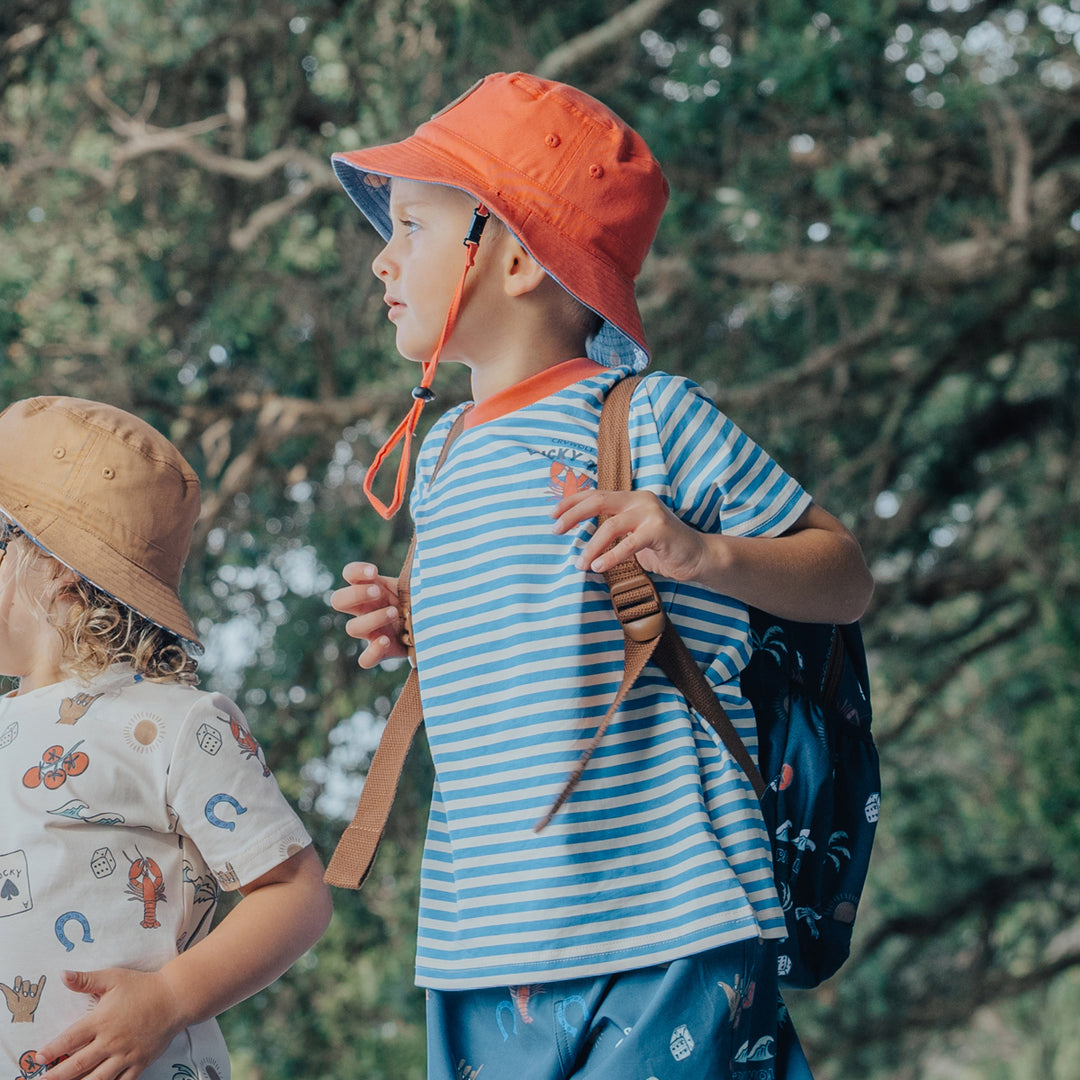 Two children outdoors with a focus on one wearing an orange hat and crywolf striped shirt.