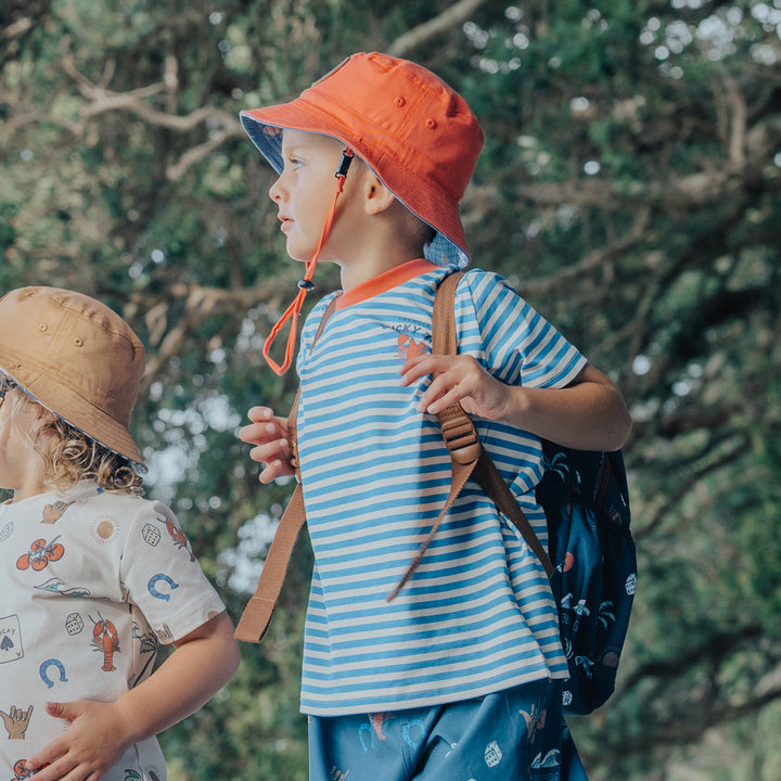 Two children outdoors with a focus on one wearing an orange hat and crywolf striped shirt.