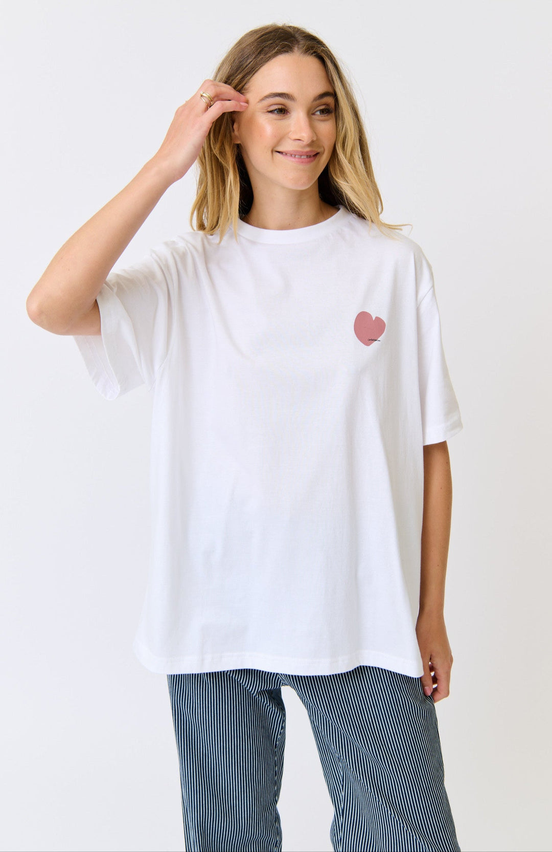 Woman wearing a white t-shirt with a pink heart design on a plain background