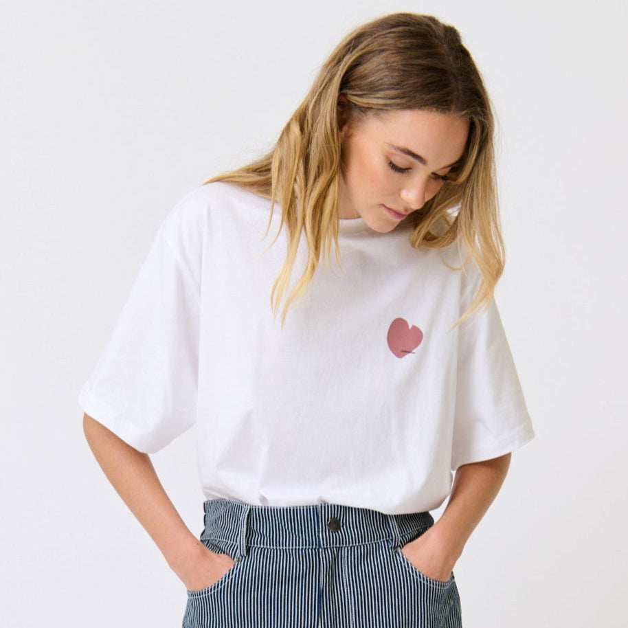 Woman wearing a white t-shirt with a red heart design and blue striped pants on a white background