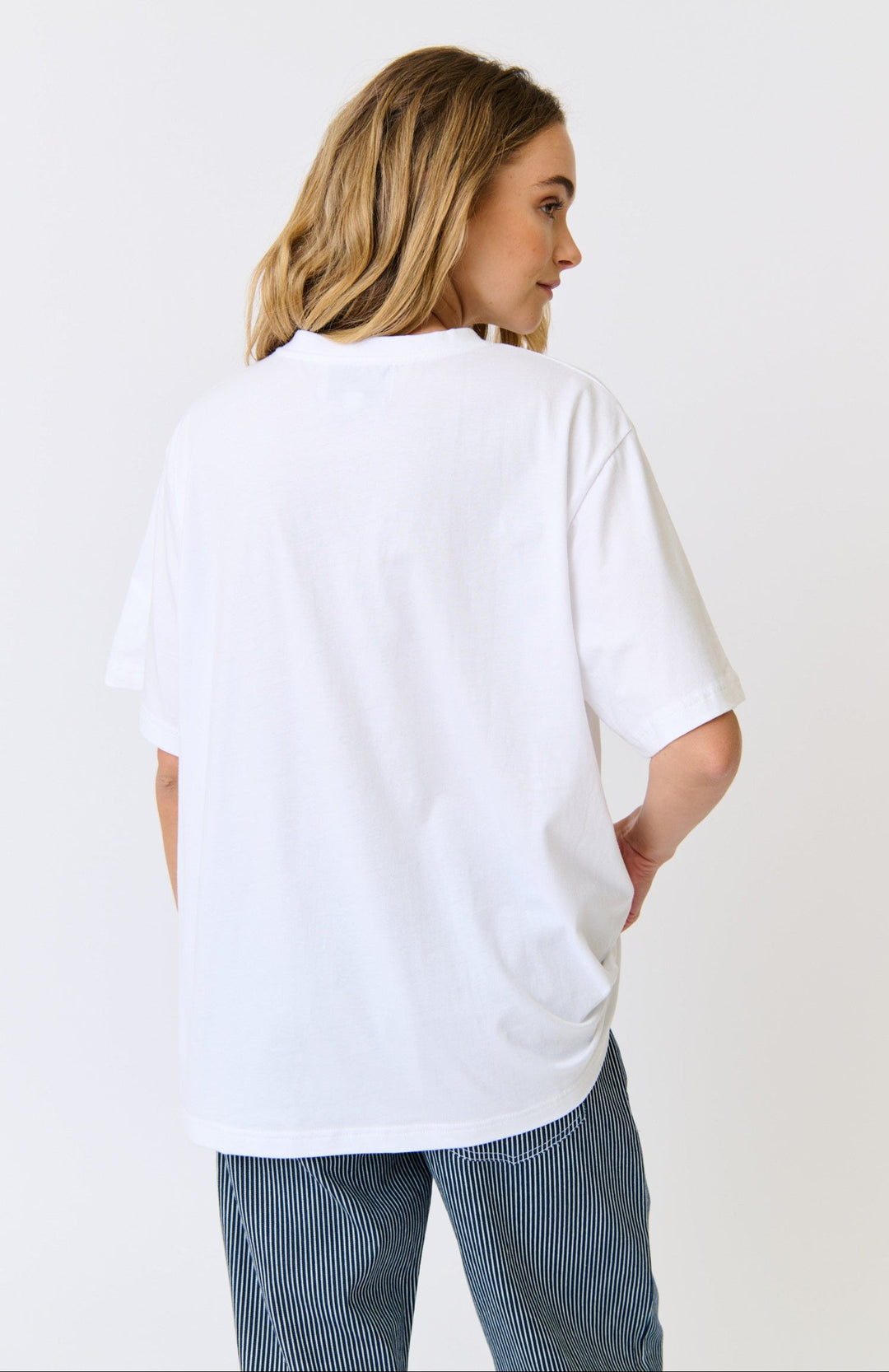 Person wearing a white oversized t-shirt and blue jeans on a plain background