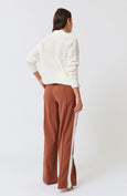Woman wearing a white knit cardigan and brown pants on a white background