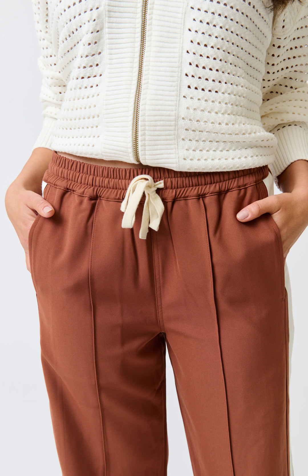 Brown pants with a drawstring and white sweater on a light gray background