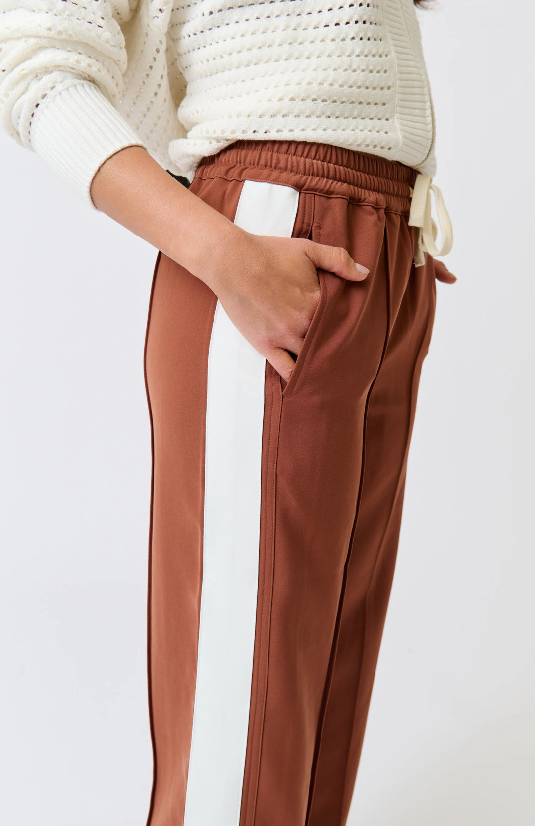 Brown pants worn with a white sweater on a light gray background
