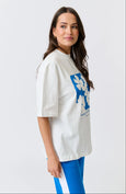 Woman wearing a white oversized t-shirt with a blue graphic design on a light gray background