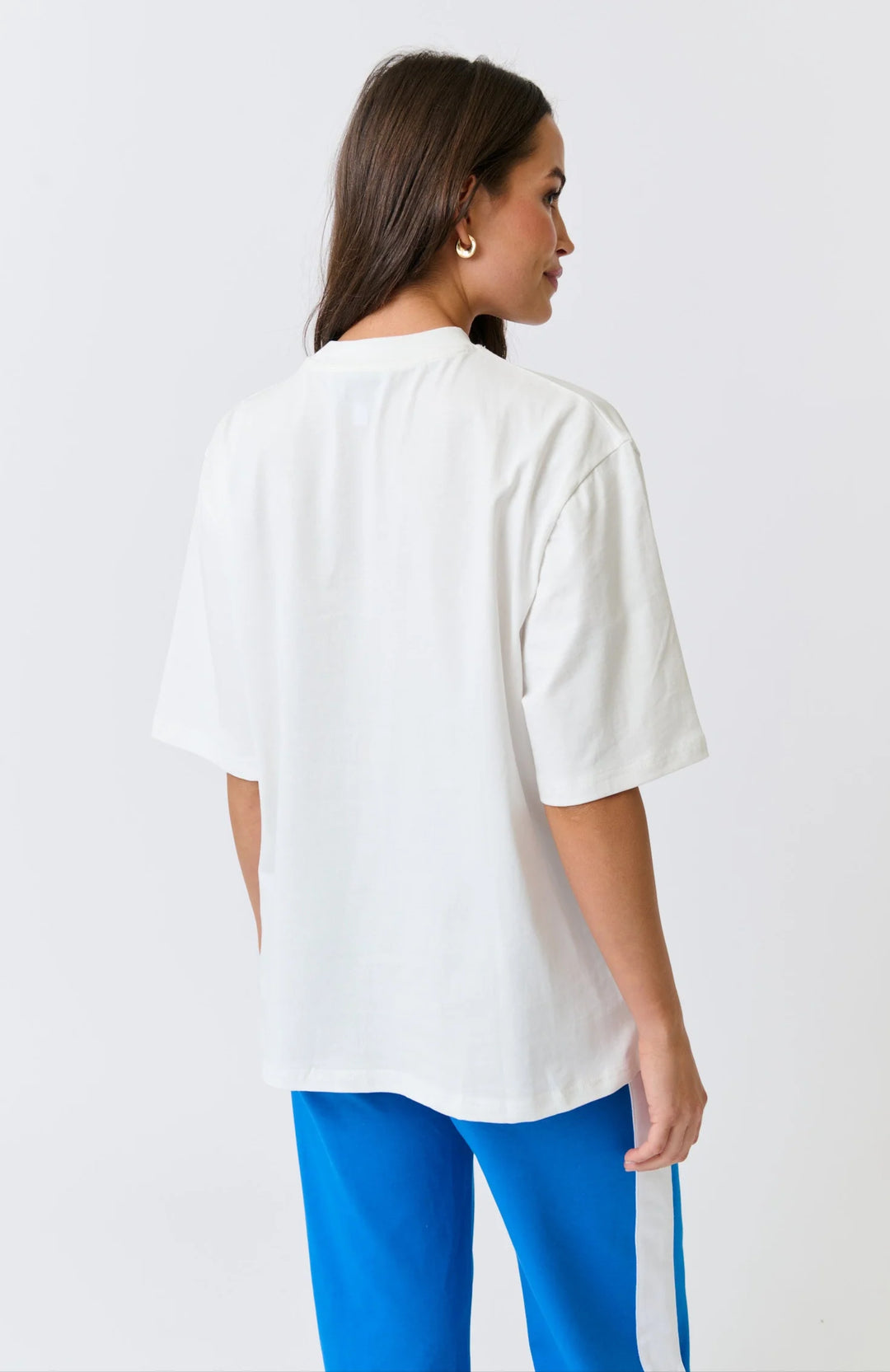 Woman wearing a white oversized shirt and blue pants on a light gray background