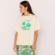 Woman wearing a cream t-shirt with green text and a green floral skirt on a white background