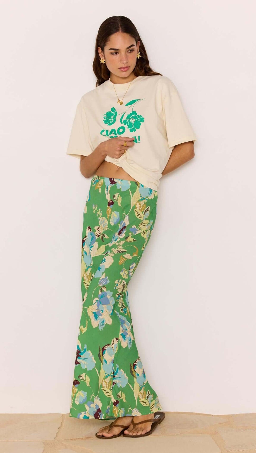 Woman wearing a cream t-shirt with green text and floral pants against a white background