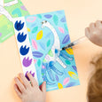 Child coloring a dinosaur picture with markers on a light brown surface