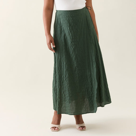 Woman wearing a white top and green isle of mine skirt on a plain background