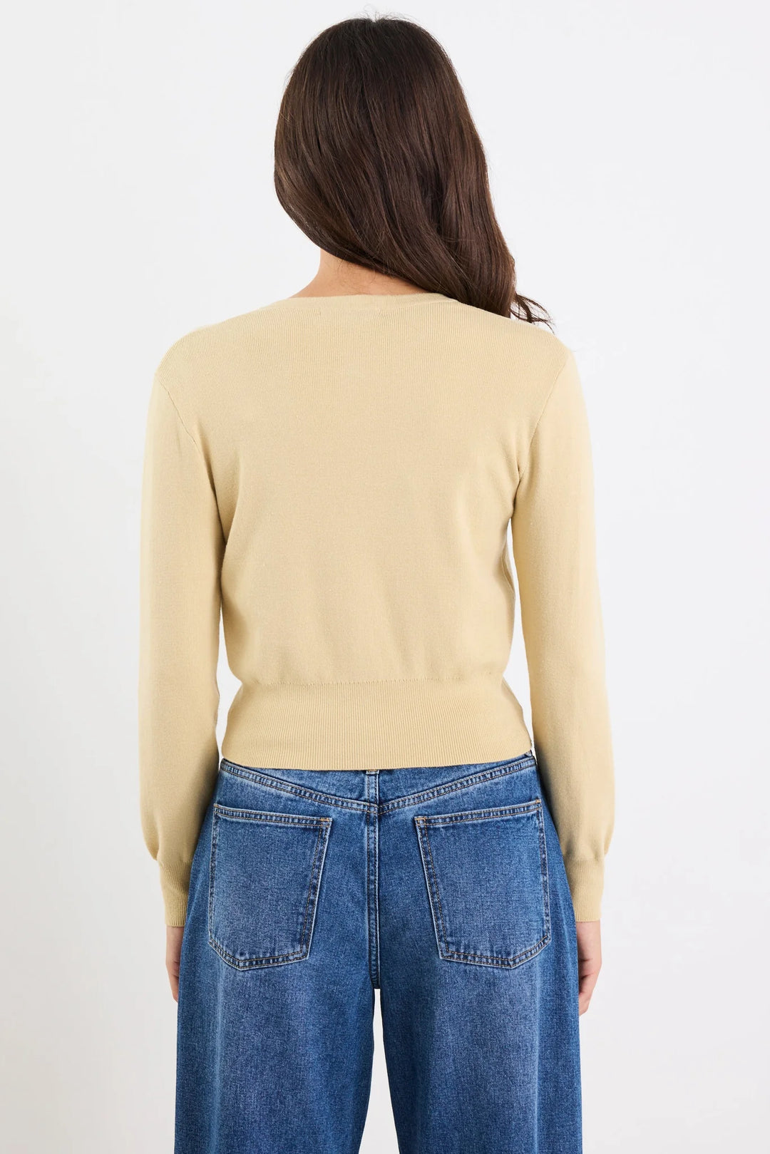 Person wearing a beige sweater and blue jeans on a white background