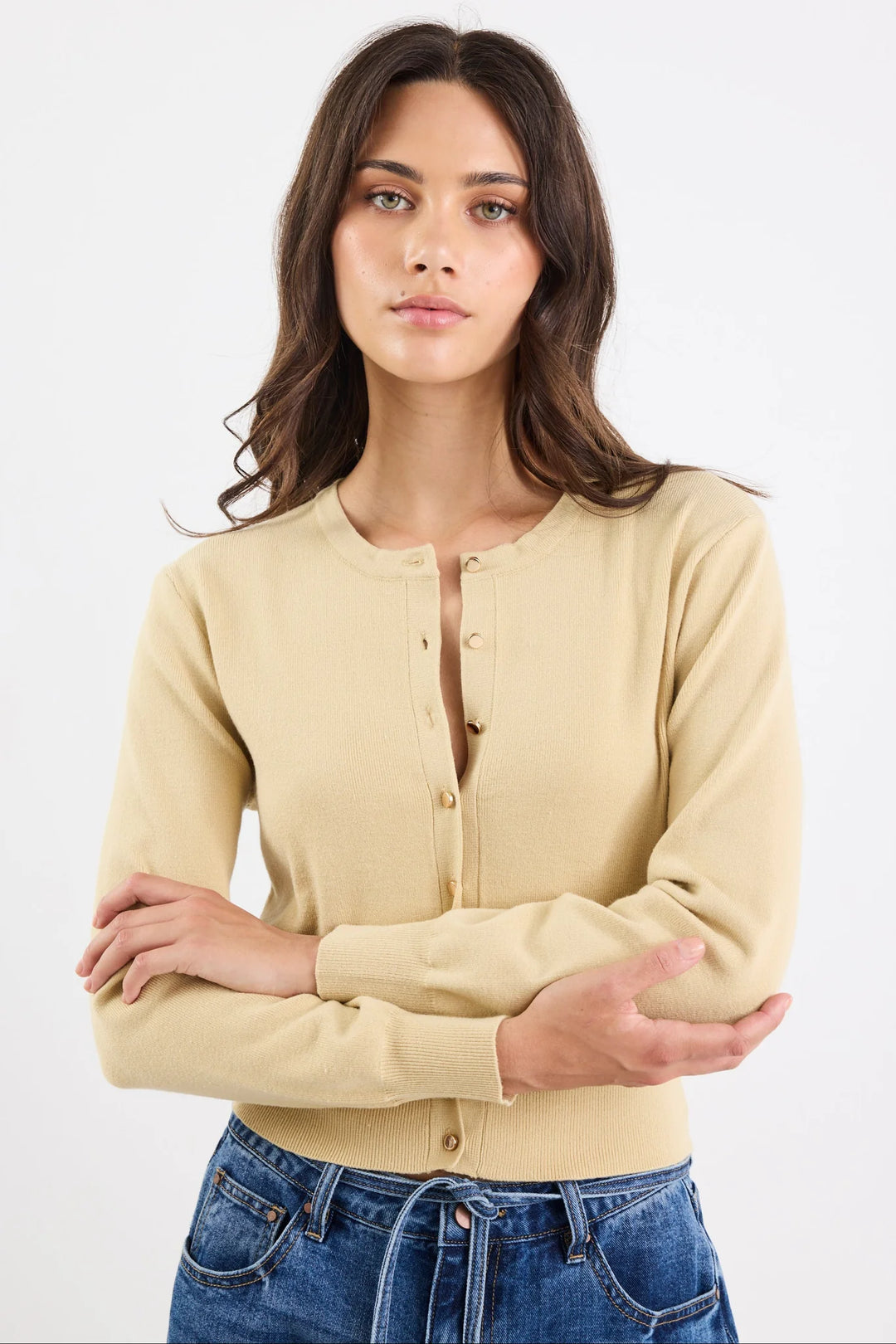 Woman wearing a light yellow cardigan over a black top with blue jeans on a white background