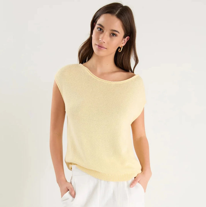 Woman wearing a yellow sleeveless top and white pants on a white background