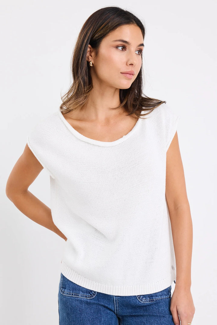 Woman wearing a white sleeveless top and blue jeans on a plain background