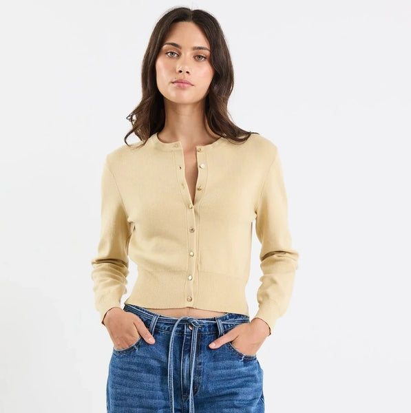 Woman wearing a light yellow cardigan, blue jeans, and white sneakers on a white background