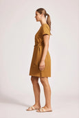 Woman wearing a eb & ive mustard yellow dress on a light pink background
