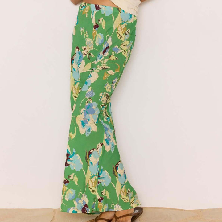 Woman wearing a cream t-shirt with green text and floral pants against a white background