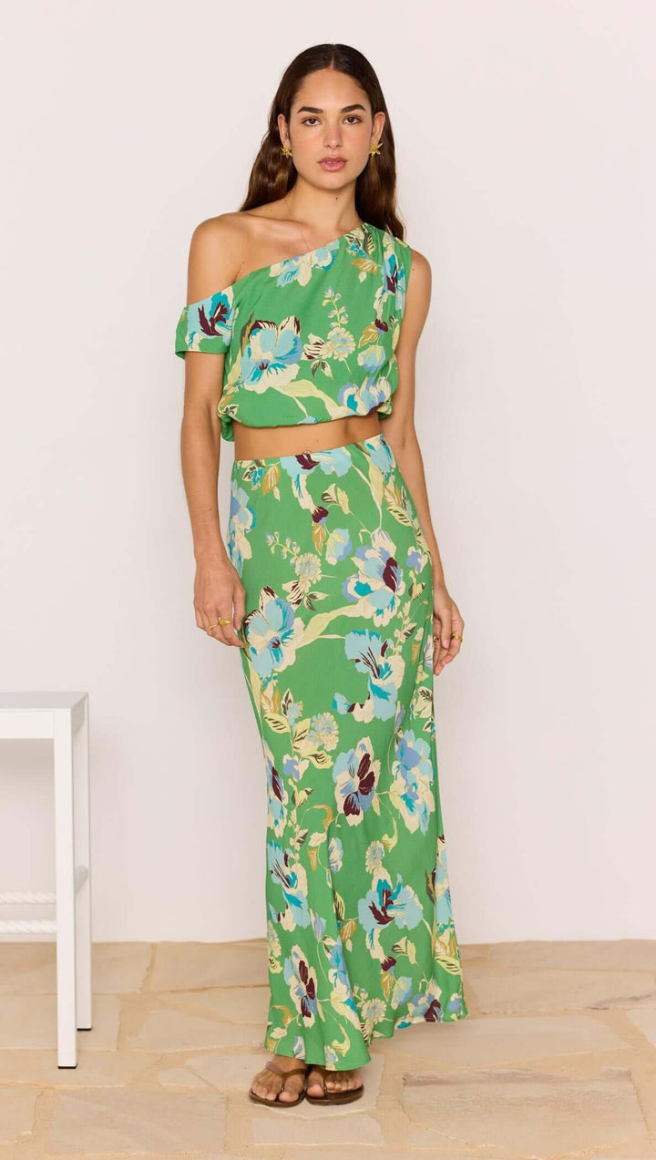 Woman wearing a green floral off-shoulder top and skirt set against a white background